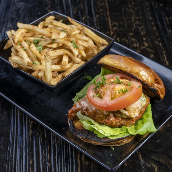 A chicken parmesan sandwich with lettuce, tomato, and fries on a black plate.