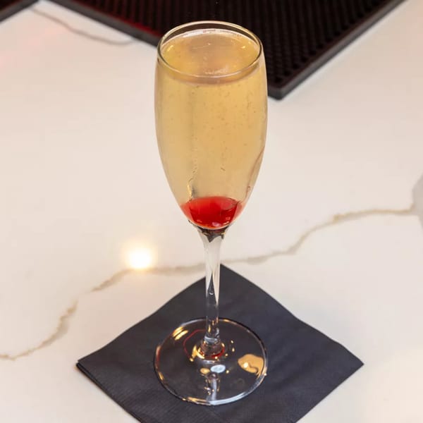 A champagne flute with a red cherry at the bottom sits on a black napkin.