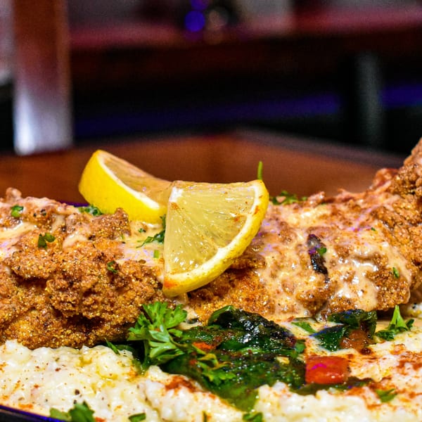 Crispy fried fish with creamy sauce, lemon wedges, and parsley over grits.